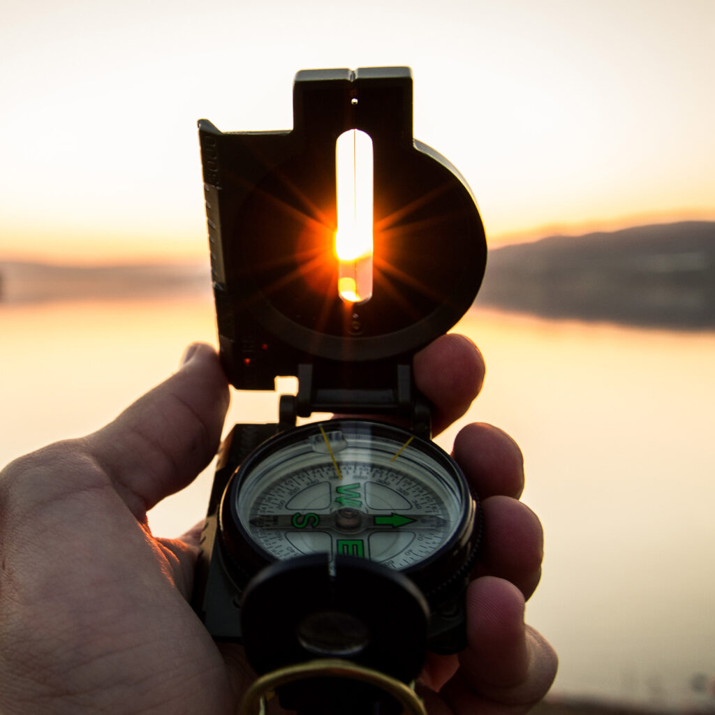 Hand holding compass toward the sunset